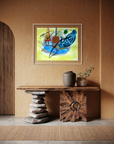An abstract framed painting with blue, yellow, green, and red brushstrokes hangs on a warm brown textured wall above a rustic wooden console table with stone and wood bases.