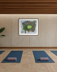 A serene indoor yoga or meditation room with four blue mats arranged on a wooden floor, each with a purple cushion. A large potted plant stands against the left wall, and a framed abstract artwork hangs centered above the mats.