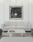 A modern living room setup featuring a white three-seater sofa centered against a white paneled wall with a framed abstract black and white print. Flanking the sofa are two dark gray armchairs, with a low white rectangular coffee table in front.