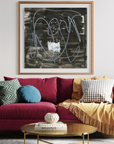 A framed abstract black and white painting hangs on a white paneled wall above a magenta sofa styled with accent pillows and a yellow throw blanket in a bright living room.