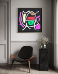 A framed abstract geometric wall art print hangs on a light gray wall above a black and wood lounge chair, next to a black marble side table with a vase of baby's breath.