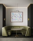 A modern interior scene featuring a curved olive green upholstered banquette seating piece around a round table, set against a light gray wall with a framed abstract geometric print and wall sconces.