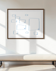 Geometric abstract artwork placed above a low bench in a minimally decorated space with dried grasses placed in a black vase. Books are placed on low table next to the vase and shadows are cast through the window as light comes in
