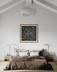A styled bedroom interior with a bed dressed in taupe and brown bedding, flanked by two matching nightstands and gold wall lamps, beneath a large framed abstract black-and-white artwork on a light gray wall. A textured white pendant light hangs from the sloped ceiling.