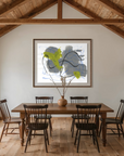 A dining room interior with a wooden dining table and six black spindle-back chairs, set under a high wood-beamed ceiling. A framed abstract print hangs on the back wall above the table, and a built-in arched niche on the right holds ceramic vases.