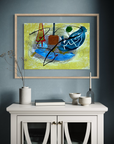 An abstract framed painting featuring blue, yellow, black, and red brushstrokes, displayed on a dark blue-gray wall above a white sideboard with decorative ceramic objects.