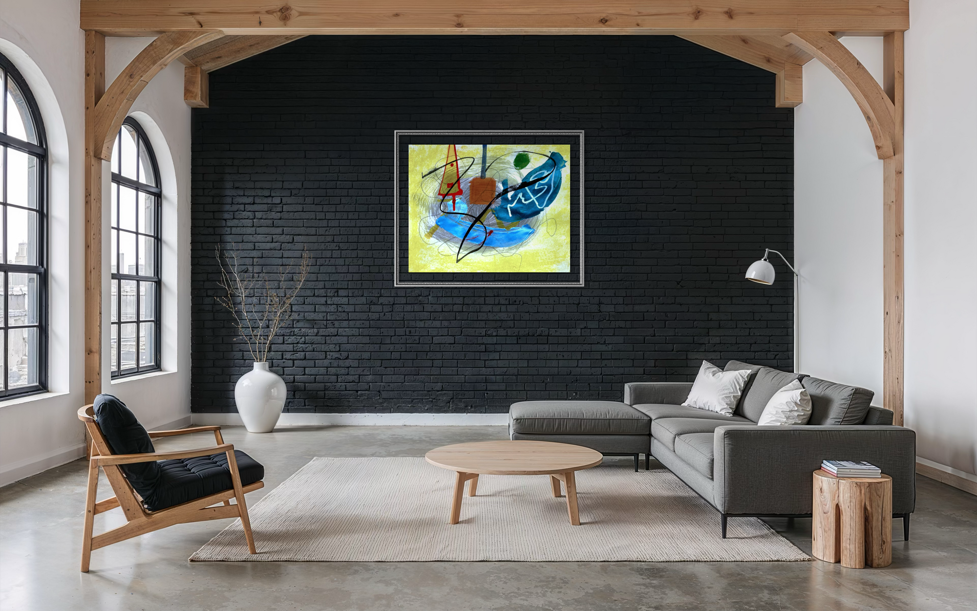 A framed abstract painting with blue, yellow, orange, and black brushstrokes hangs on a black brick wall in a modern loft-style living room with a gray sectional sofa, wooden chair, and exposed wood beams.