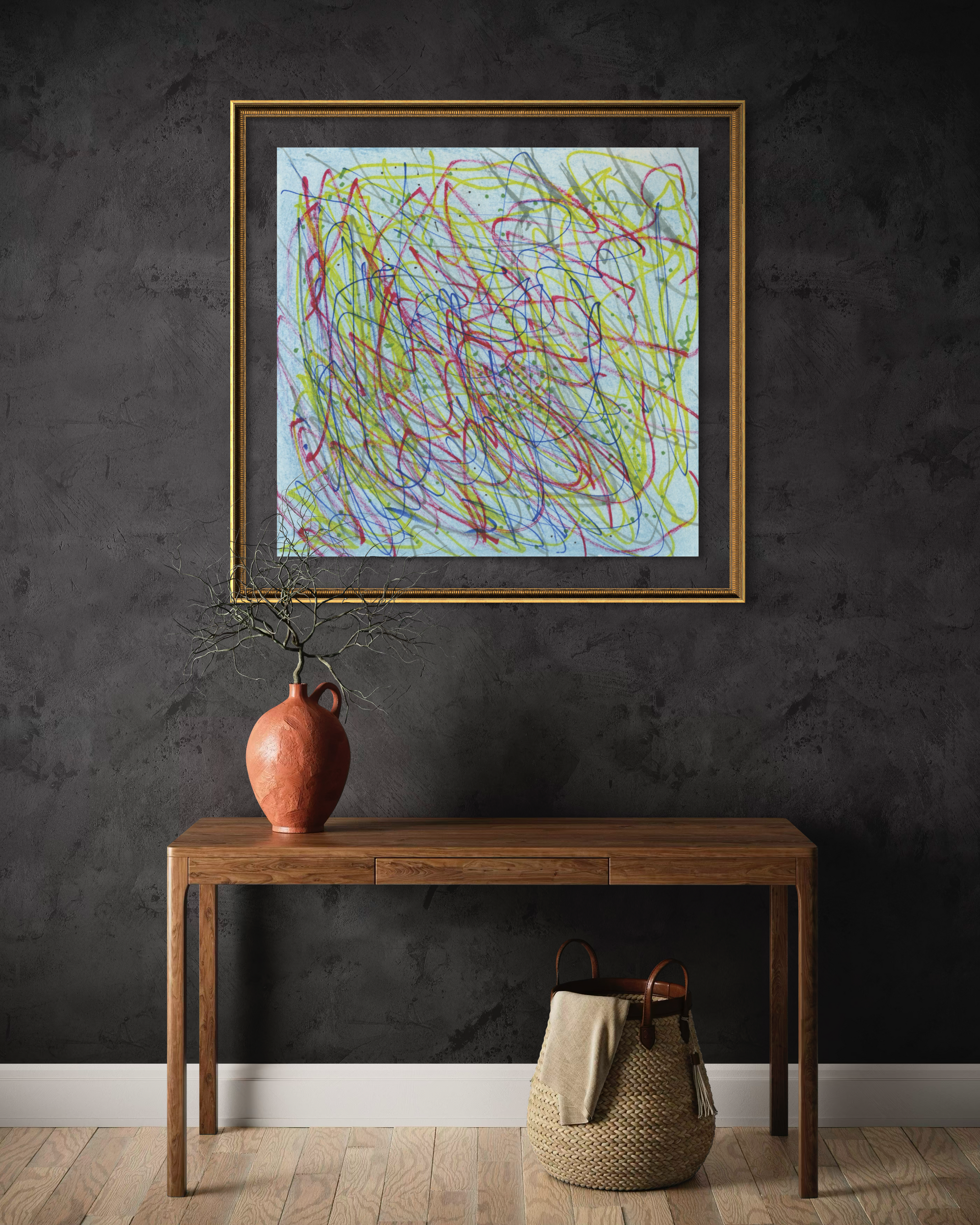 A framed abstract art print featuring colorful scribbled lines on a light blue background, hung on a dark textured wall above a wooden console table with a terracotta vase and a woven basket.