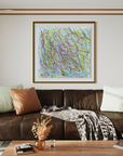A framed abstract art print with multicolored scribbled lines hangs on a white wall above a brown leather sofa in a modern living room setting.