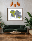 A framed abstract art print featuring gray, black, and lime green shapes, displayed on a textured white wall in a modern living room setting with a green sofa, plants, and wooden flooring.