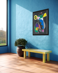 A framed abstract geometric art print hangs on a bright blue wall in a modern room setting with a yellow bench and a potted plant.