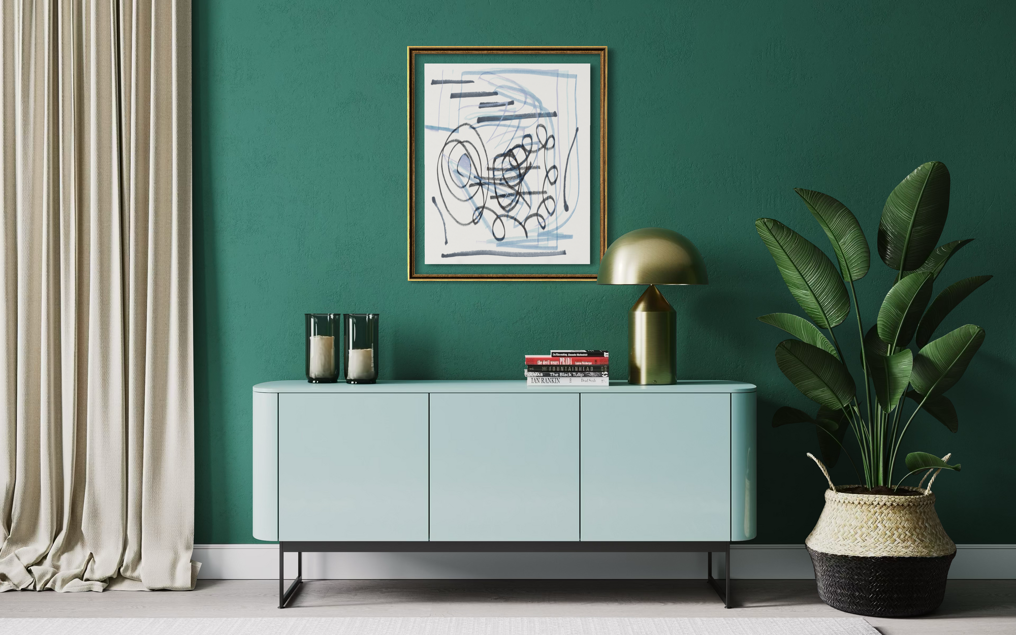 A styled interior scene with a mint green sideboard cabinet against a deep green wall, topped with a framed abstract print, a gold dome lamp, candles, and books. A large potted plant in a woven basket sits to the right, and cream curtains hang on the left.