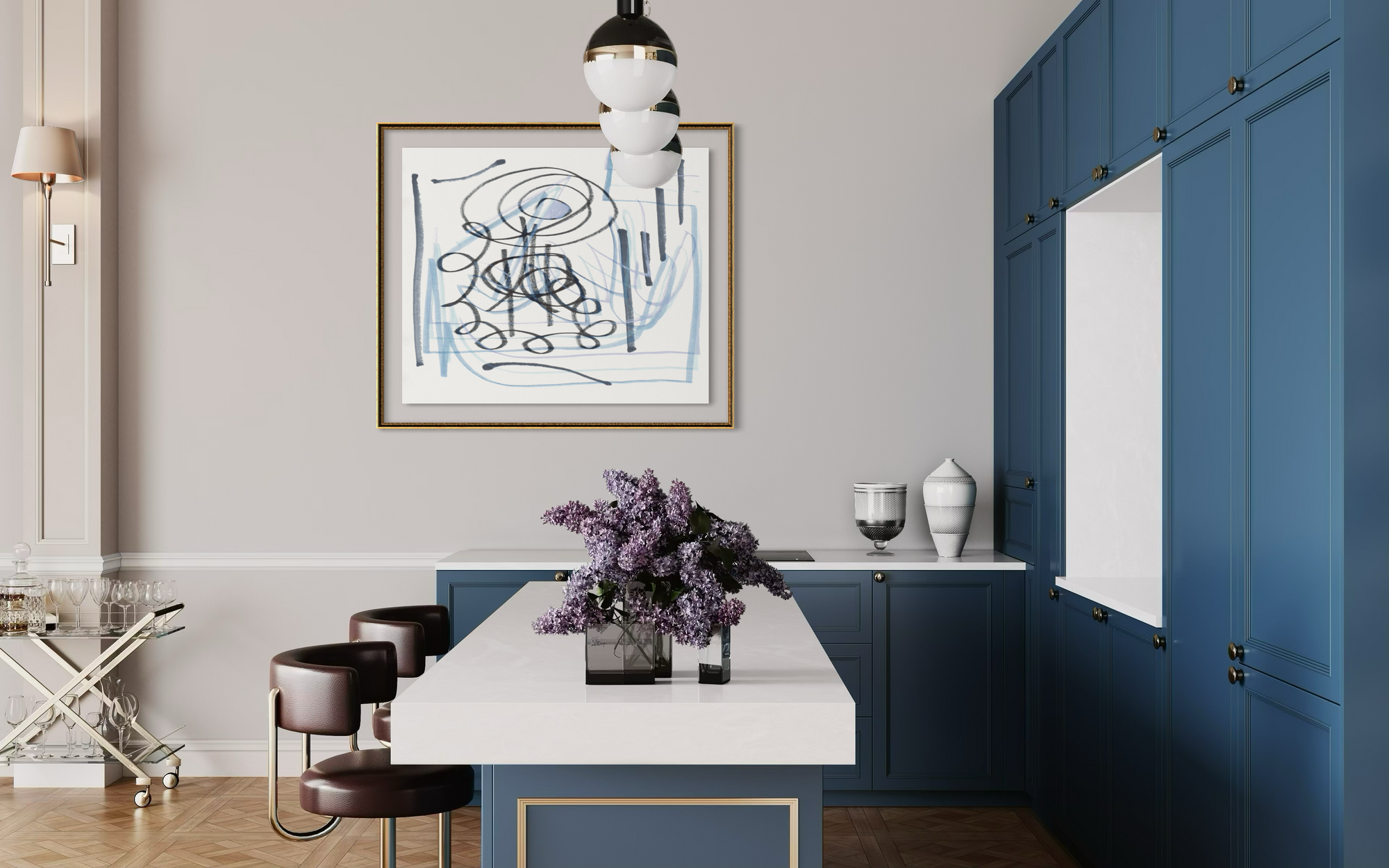 A framed abstract art print with blue and black scribbles on a white background, hanging on a light gray wall in a modern kitchen with blue cabinets and a white island.