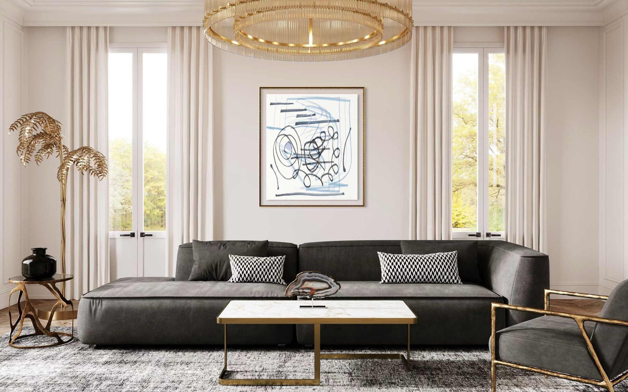 A framed abstract art print with blue and black lines on a white background, hanging on a beige wall in a modern living room with a dark gray sectional sofa, gold-framed coffee table, and large windows.
