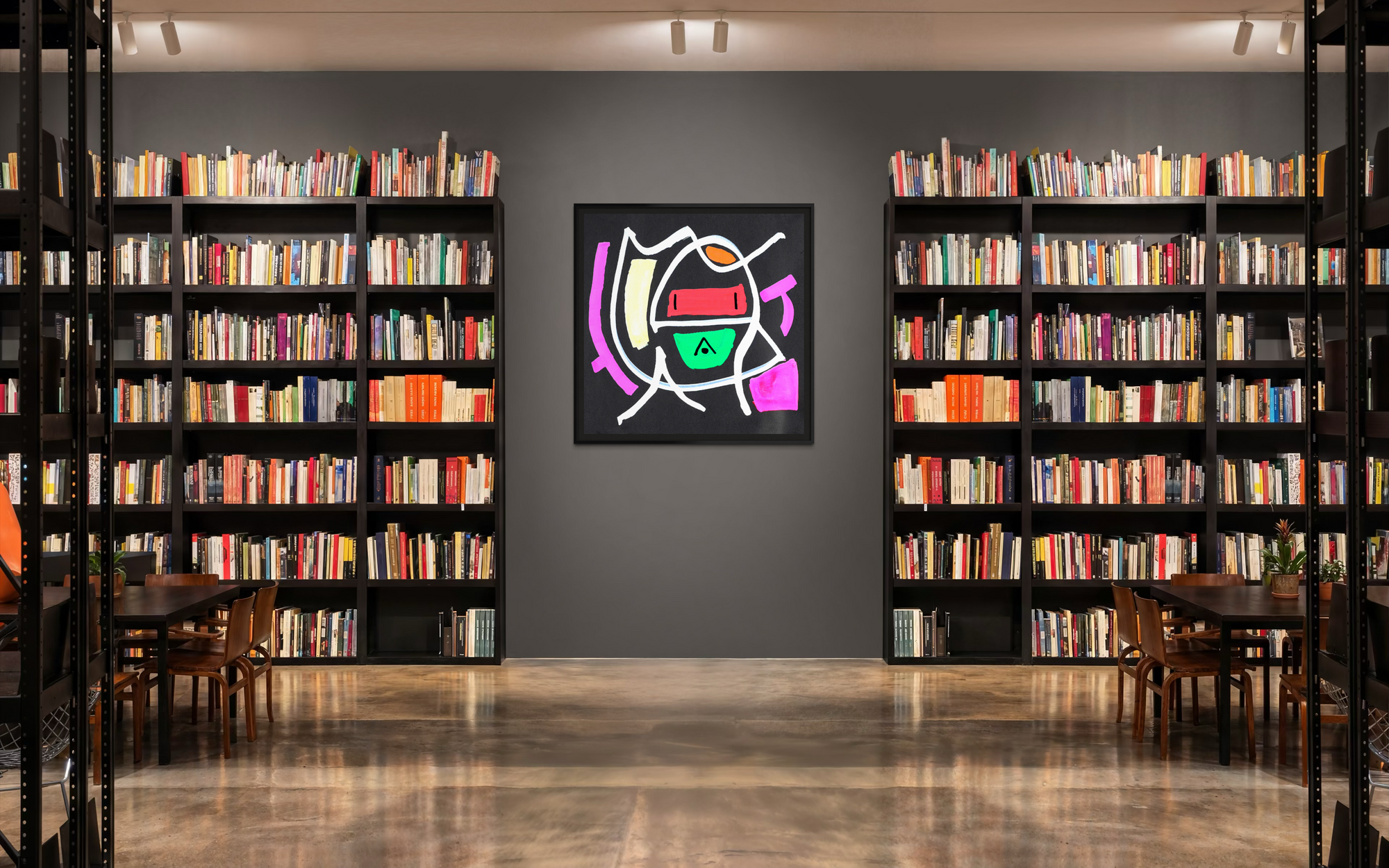 A framed abstract geometric art print hangs on a dark gray wall in a modern library or study, flanked by tall black bookshelves filled with books.