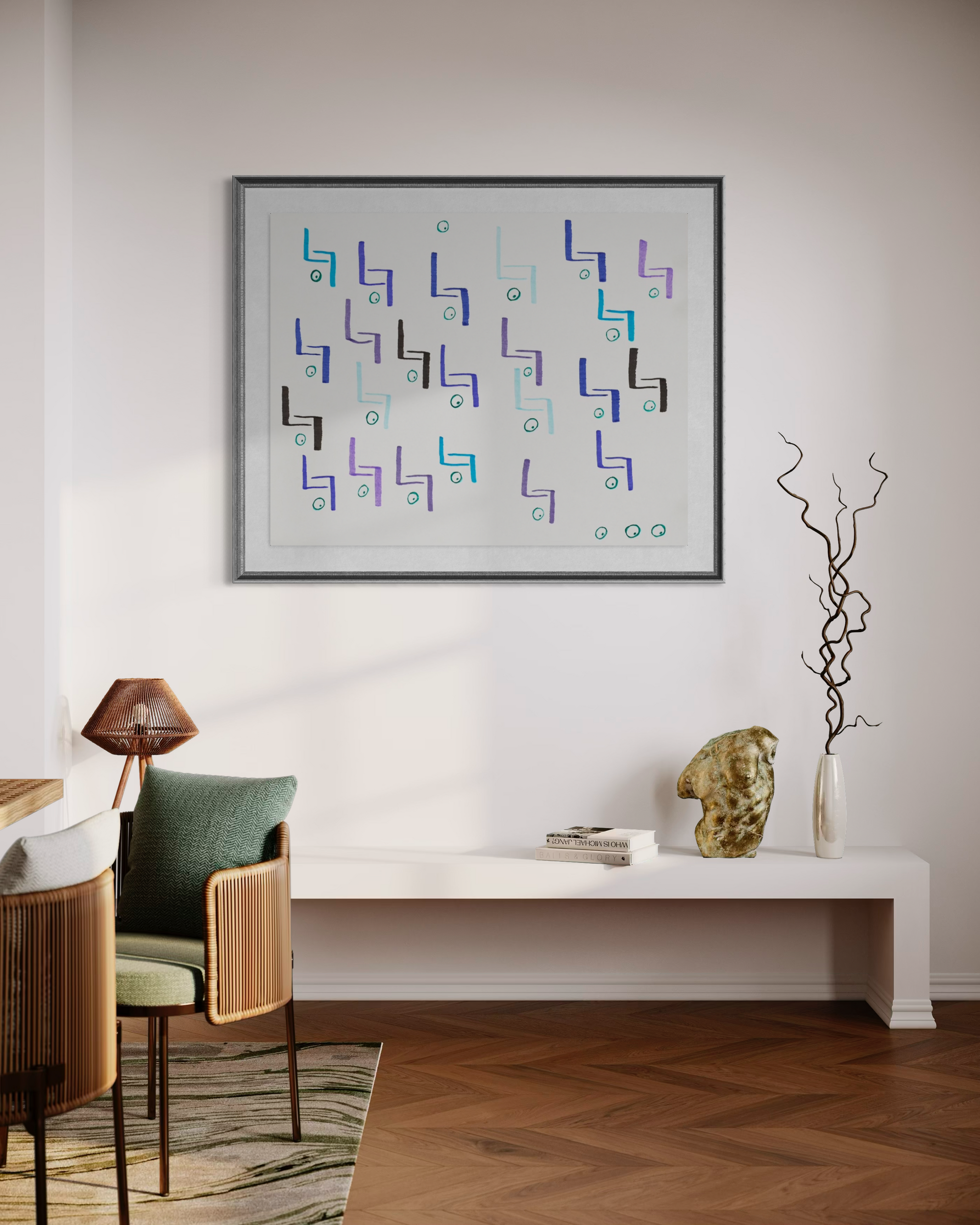 A framed abstract geometric wall art print hangs on a white wall above a long white bench in a styled room with a chair, lamp, books, and decorative branches.