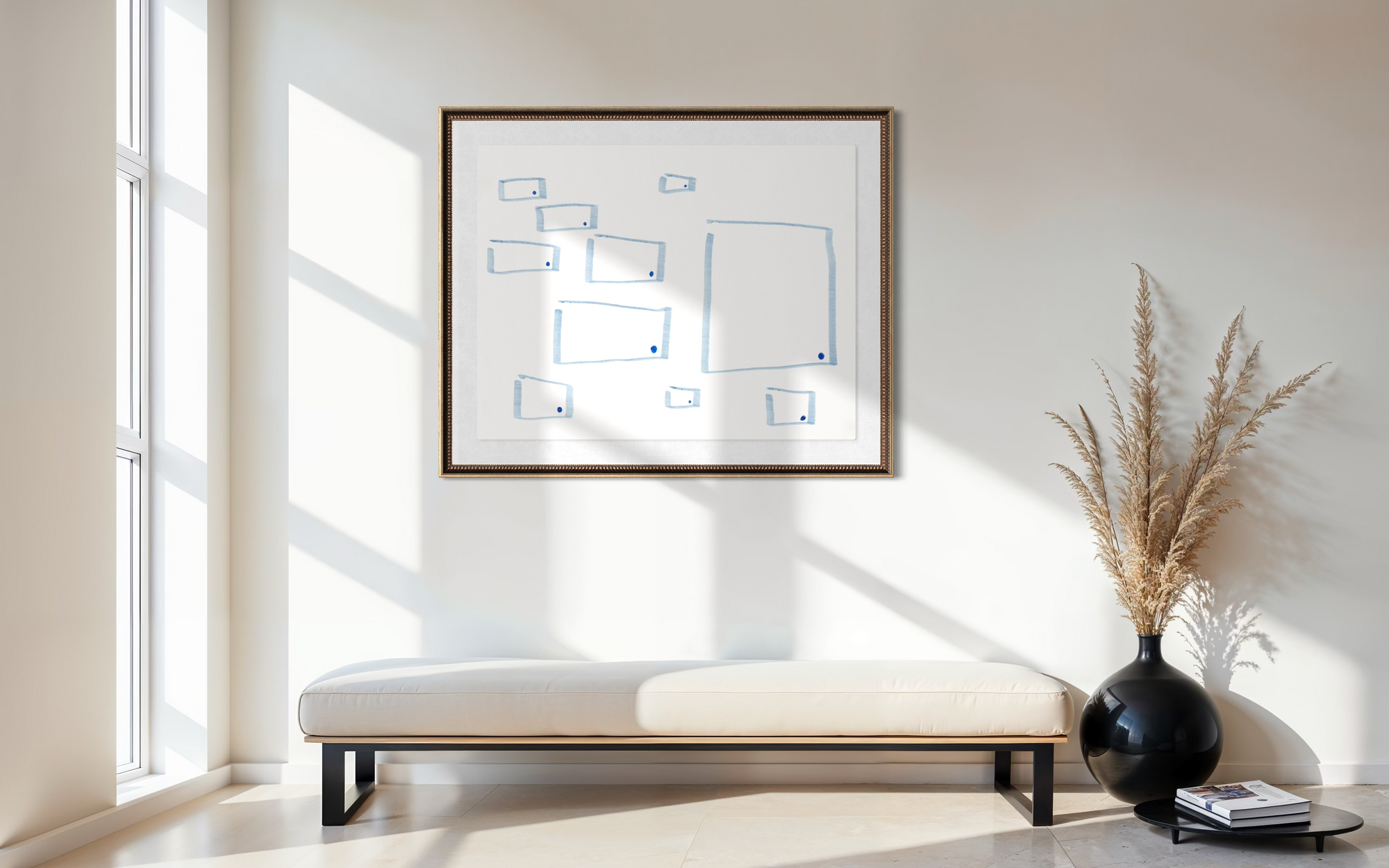 Geometric abstract artwork placed above a low bench in a minimally decorated space with dried grasses placed in a black vase.  Books are placed on low table next to the vase and shadows are cast through the window as light comes in