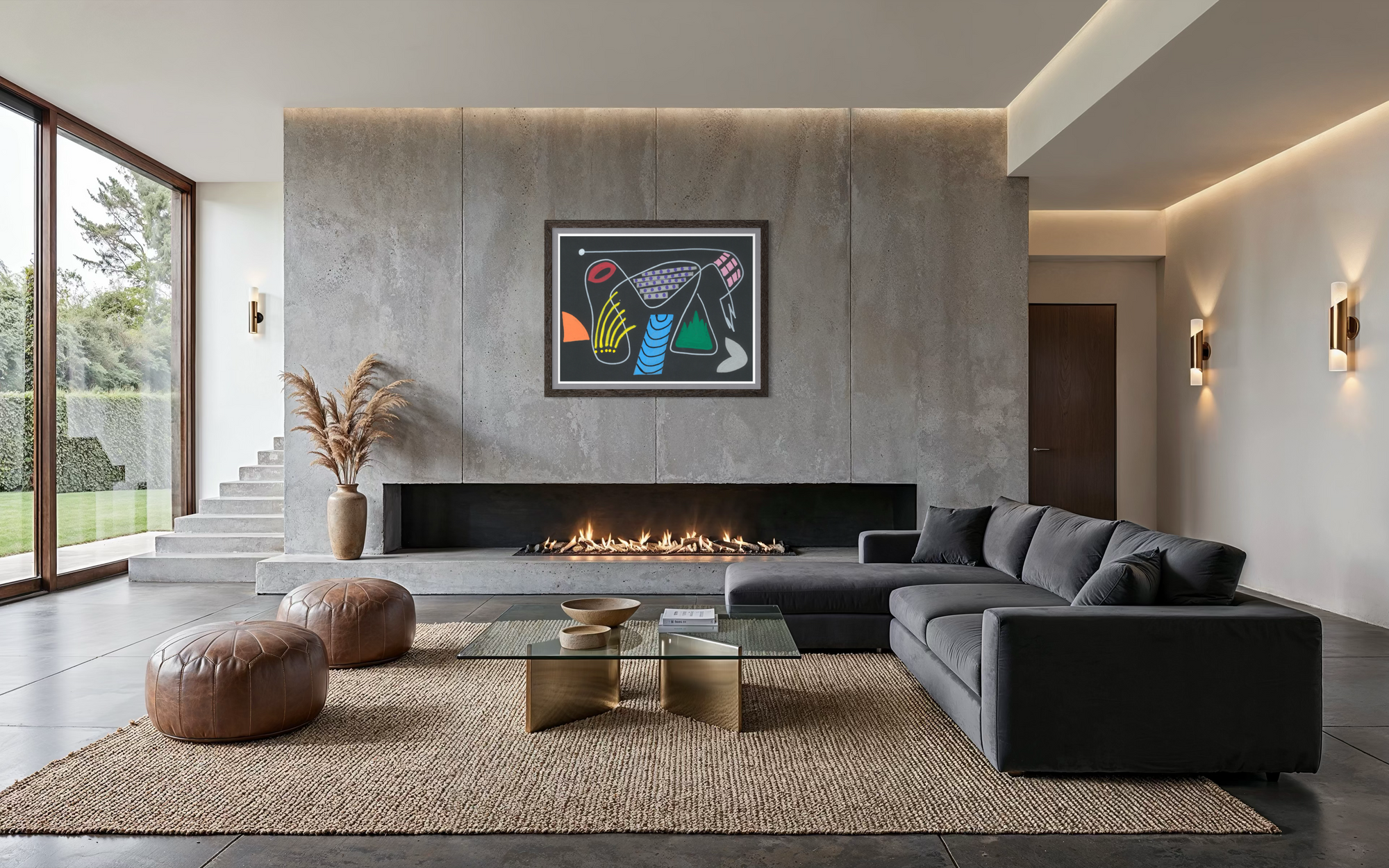 A modern living room featuring a large concrete fireplace wall with a colorful framed abstract artwork, a dark gray sectional sofa, brown leather poufs, and a glass-top coffee table on a woven rug.