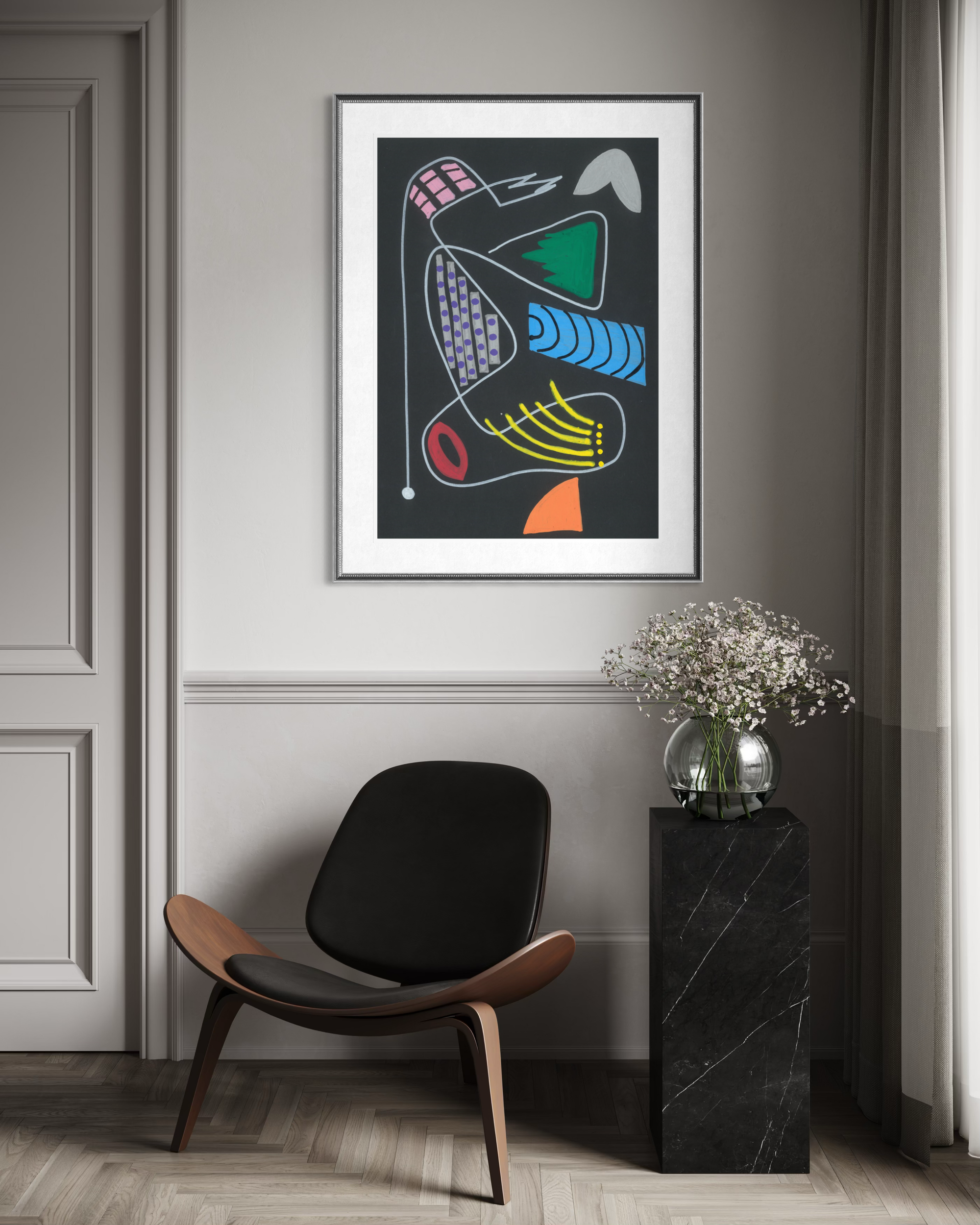 A framed abstract art print with colorful organic shapes on a dark background, displayed on a gray wall in a modern room setting above a black chair and next to a black marble side table with a vase of flowers.