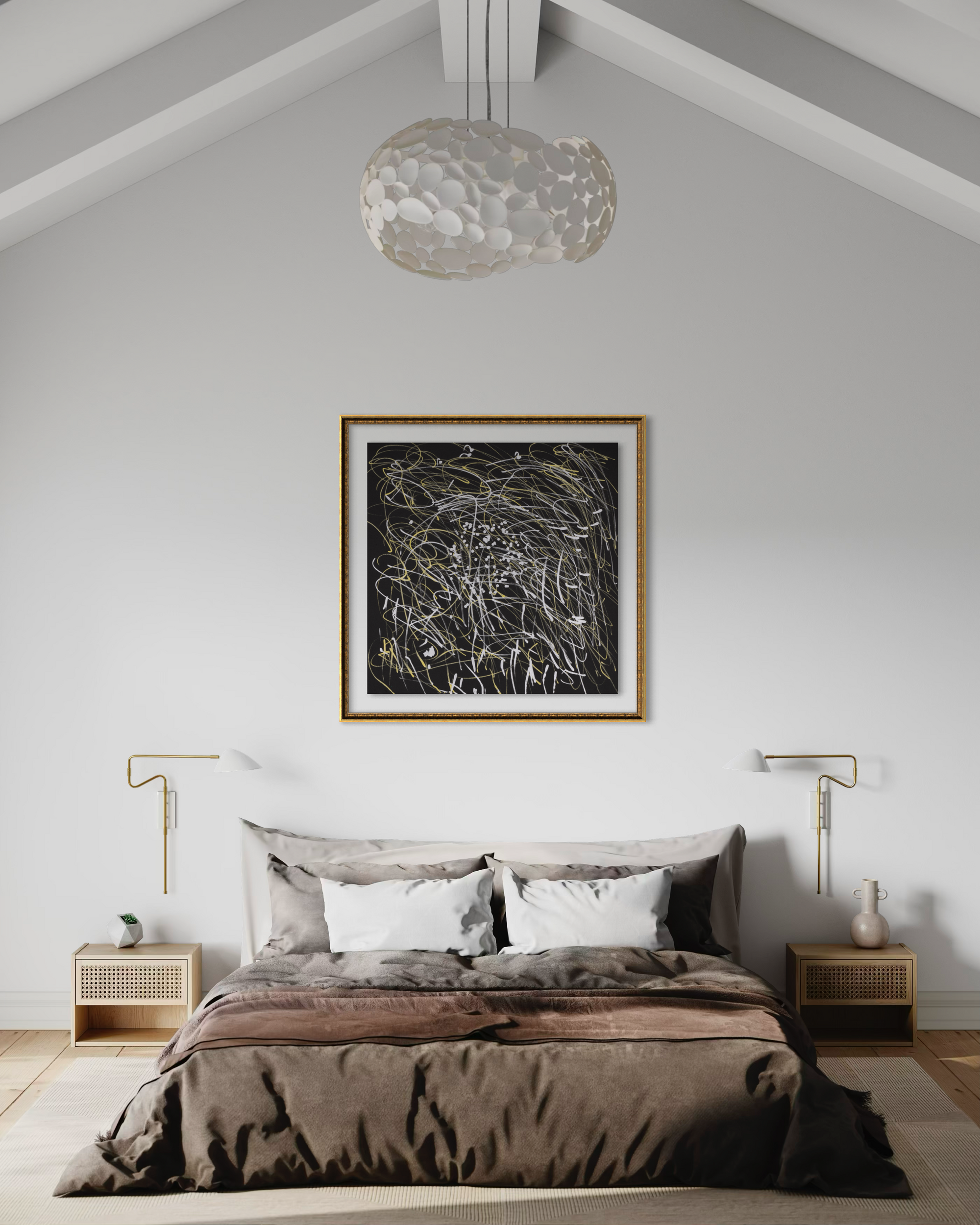 A styled bedroom interior with a bed dressed in taupe and brown bedding, flanked by two matching nightstands and gold wall lamps, beneath a large framed abstract black-and-white artwork on a light gray wall. A textured white pendant light hangs from the sloped ceiling.
