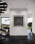 An abstract black and white painting with gold lines in a gold frame, displayed on a white wall in a modern, stylishly decorated home interior with a spiral staircase and marble floors.