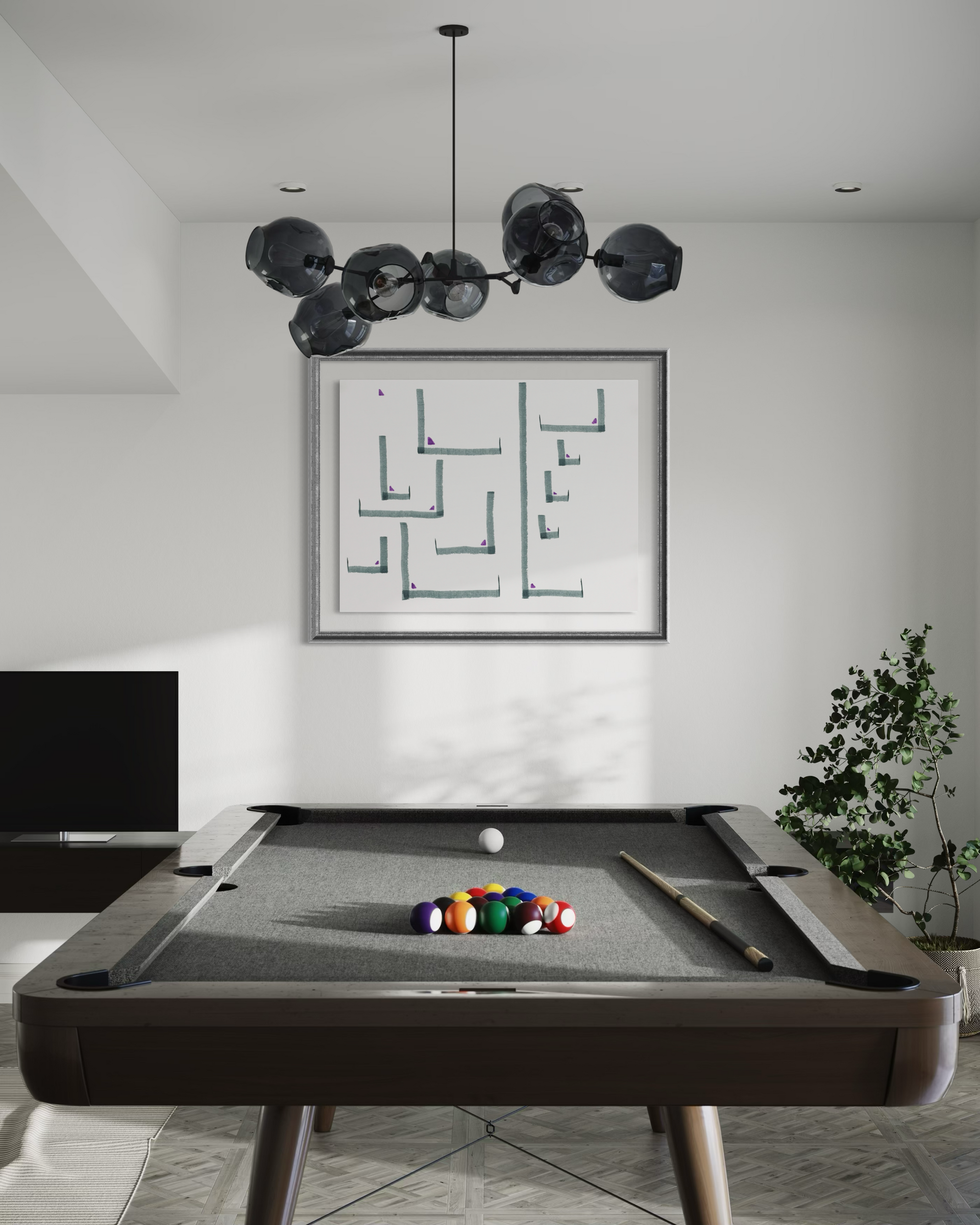 A modern pool table in a minimalist room setting, featuring a dark wood frame, gray felt surface, a rack of colorful billiard balls, a cue stick, and a white cue ball. Above the table hangs a black multi-globe chandelier, and a framed abstract print is mounted on the white wall behind it.