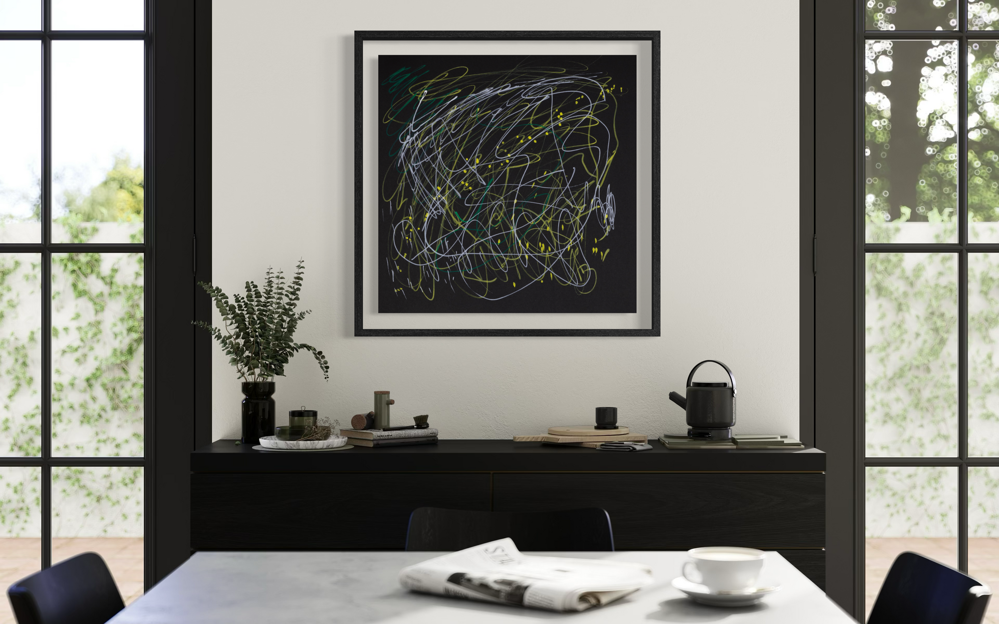 A framed abstract art print with chaotic white, yellow, and green scribbled lines on a black background, hanging on a white wall above a dark wooden console table in a modern dining room setting.